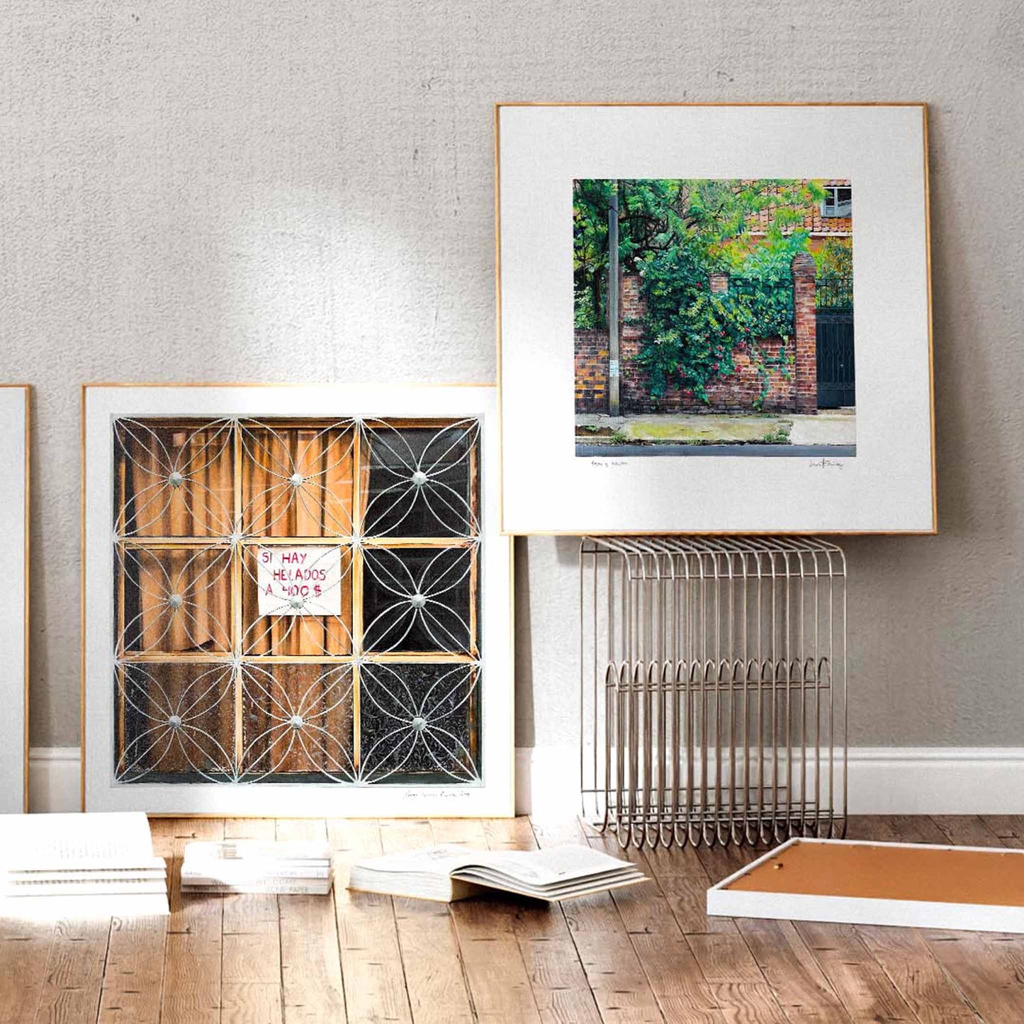 Two large square art prints in a modern studio space. One print of a window grille and one of a city.