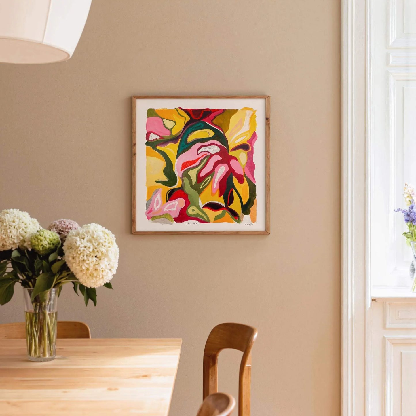 Dining room with a colorful abstract painting on the wall, a table with flowers, and a chair.