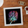 Unframed botanical art wall print of a clover flower on a wooden desktop.