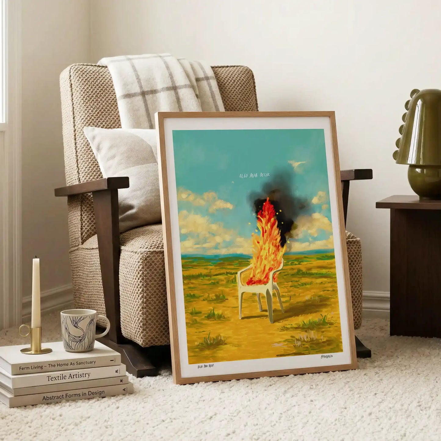Framed artwork of a burning chair in a field leaning on an armchair in a living room.