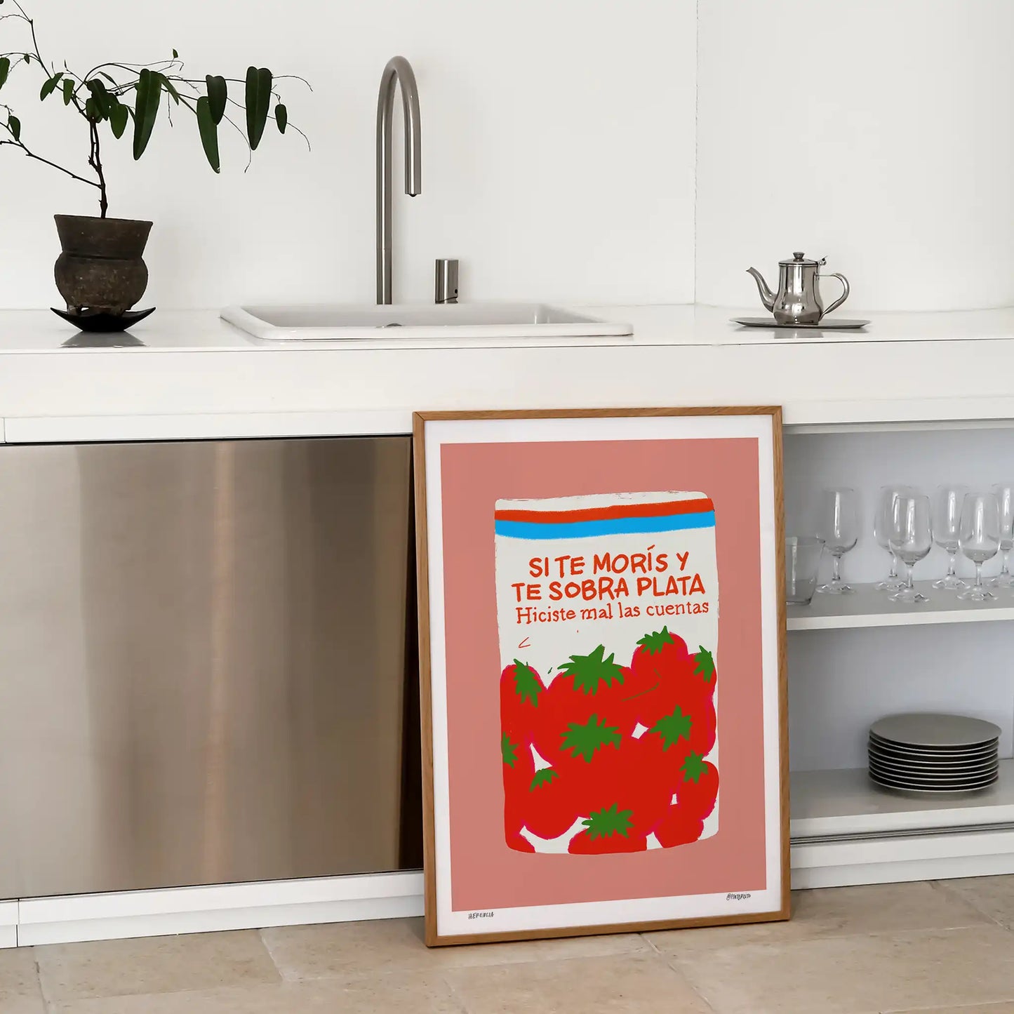 Framed art print of a tin of tomatoes on a pink background framed in wood and leaning against cabinets in modern kitchen