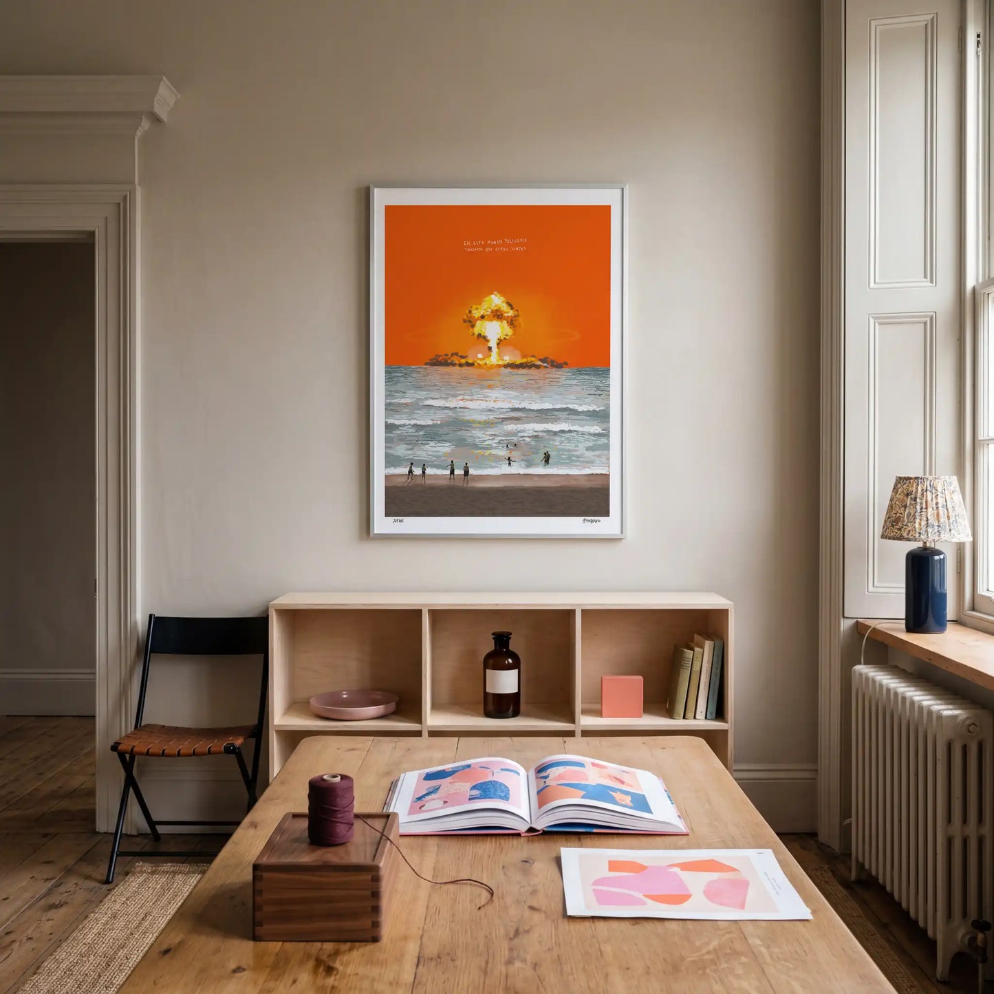 Contemporary interior with a table, books, and a large framed art print by Damian Lluvero on the wall.