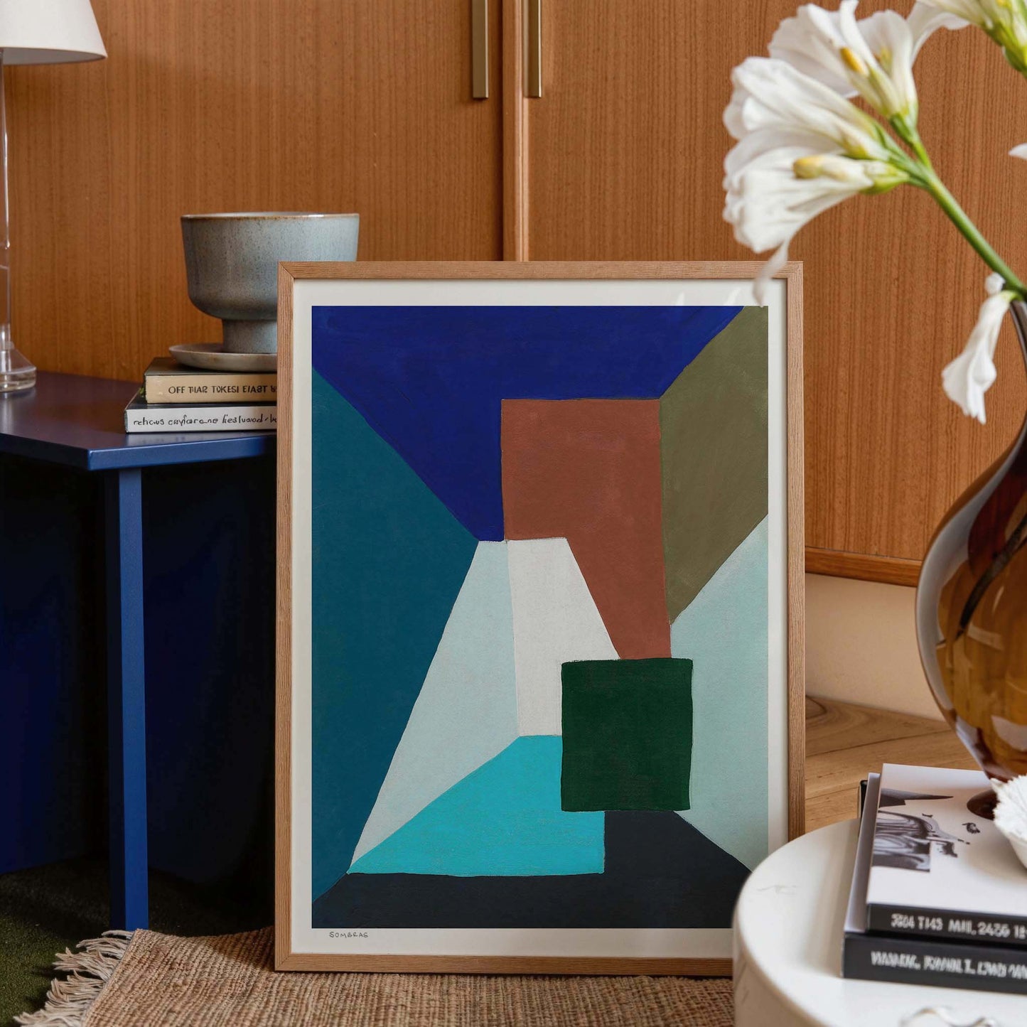 Framed abstract art print propped against a side table with decor items.