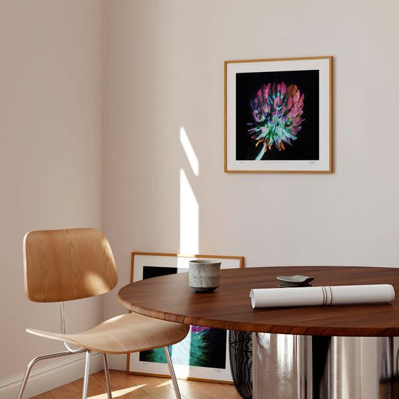 Square botanical wall art print in a neutral contemporary interior with a wooden table and chair.