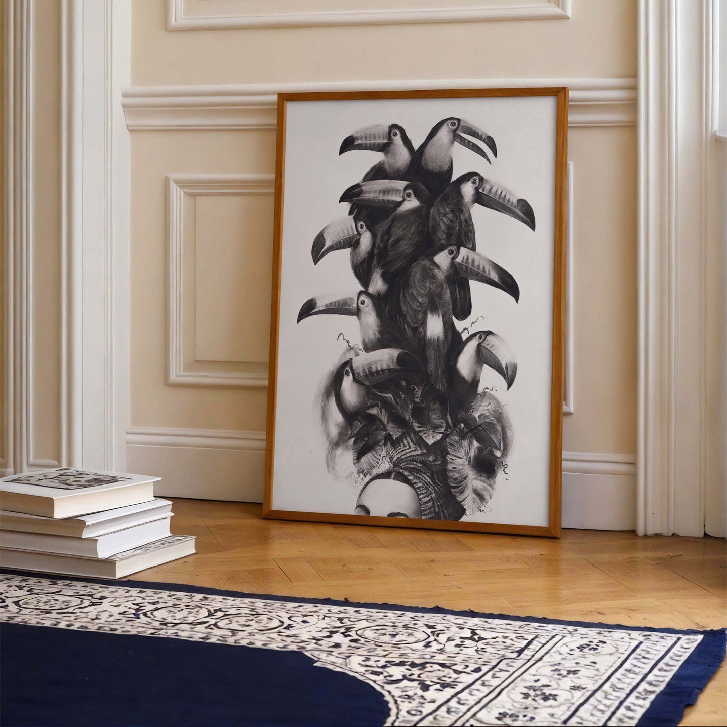 Framed artwork of toucans leaning against a wall in a room with books and a rug.