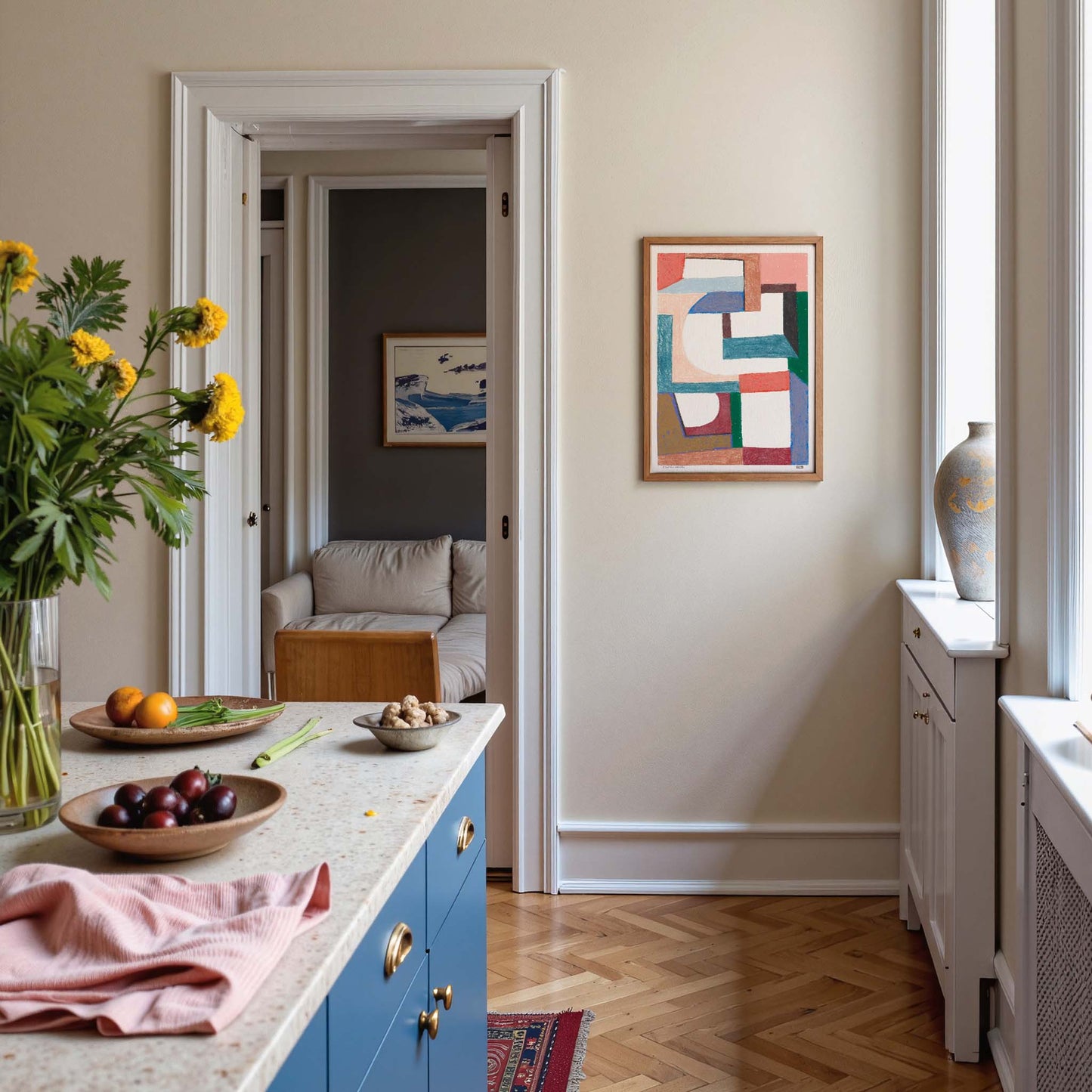 Modern kitchen with blue cabinets, a countertop with fruit and flowers, and abstract art on the wall.