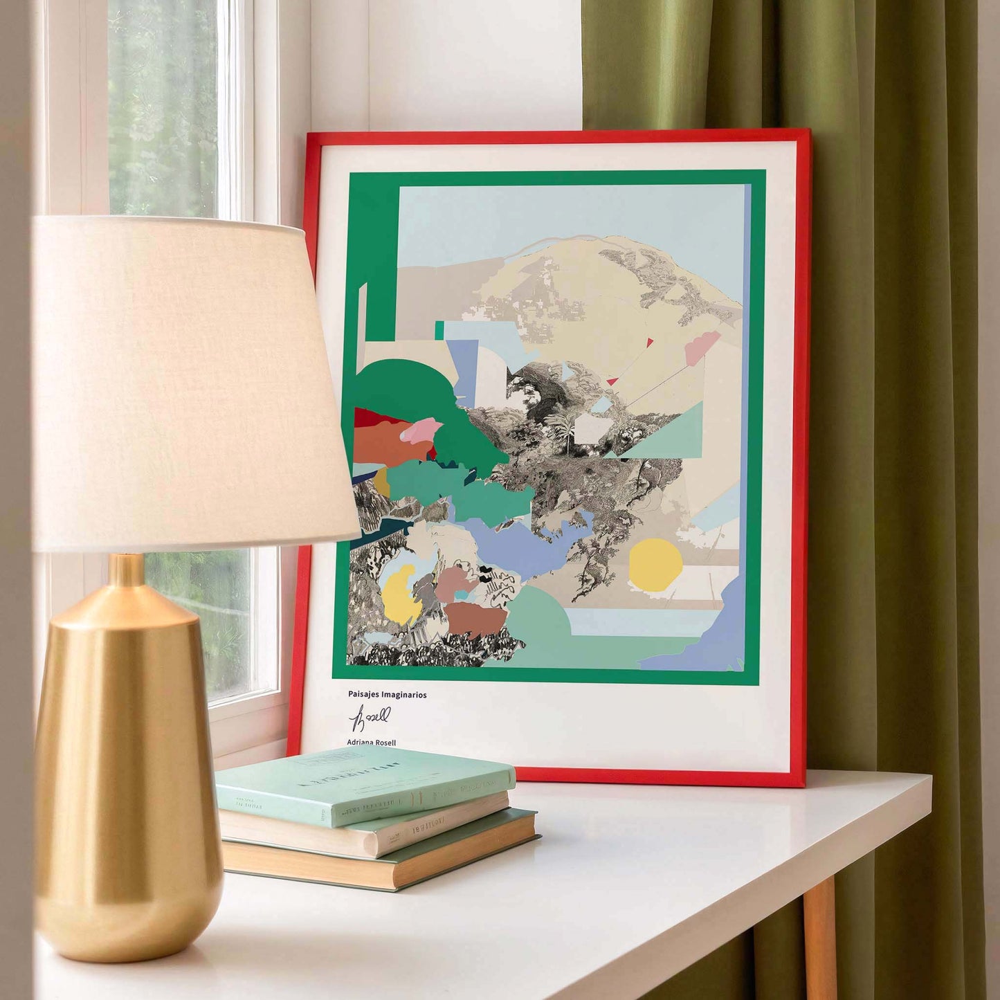 Framed landscape artwork on a windowsill with a lamp and books in a room setting