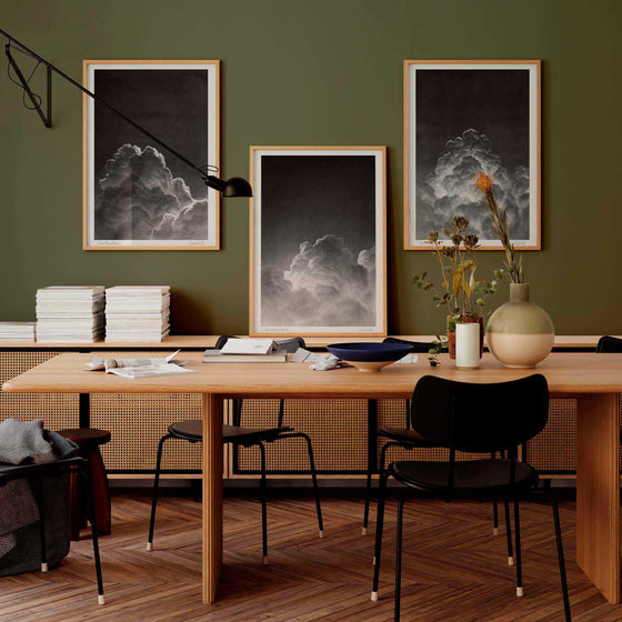Set of three black and white wall art prints of clouds on a dark wall in a modern office.