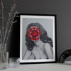 Modern wall art print of a lady with a red jewel covering her face framed against a black wall.