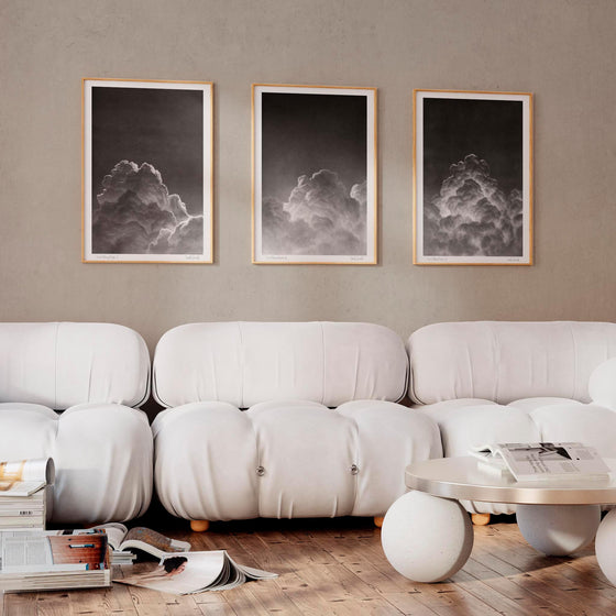 Set of three monochrome wall art prints of clouds in a neutral living room.