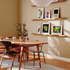 Framed gallery wall art prints displayed on shelves in a modern dining room.